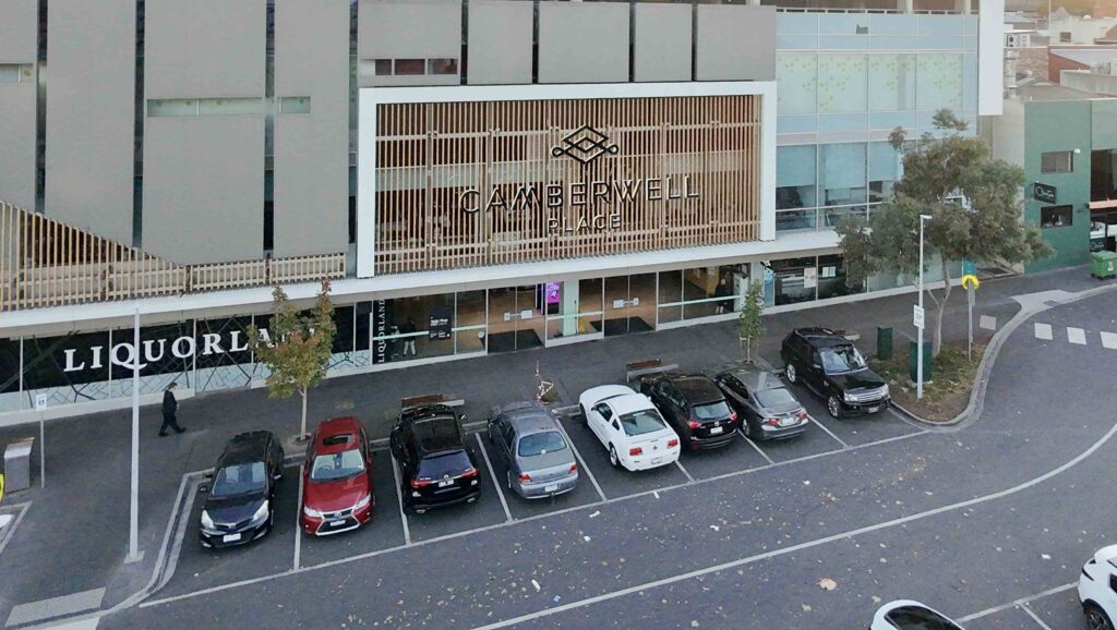 The modern architectural entrance to the Camberwell Place shopping centre, viewed from across the street-level car park.