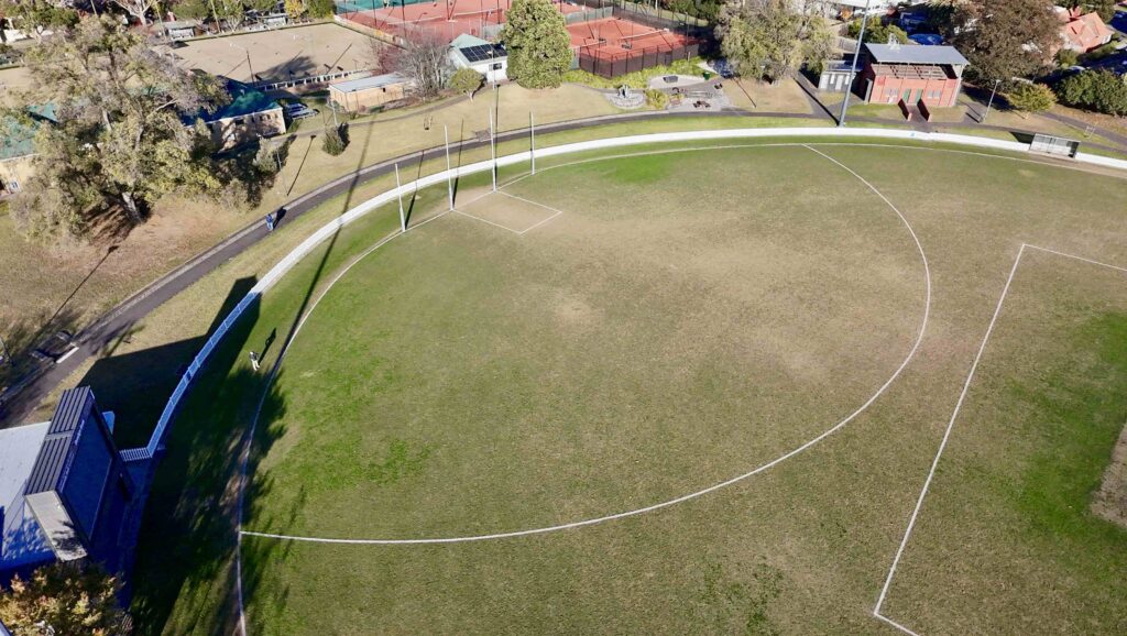 A high-angle aerial view of the complete Burke Place streetscape, showing the pixelated stone pattern from Eigen Stones flowing between green spaces.