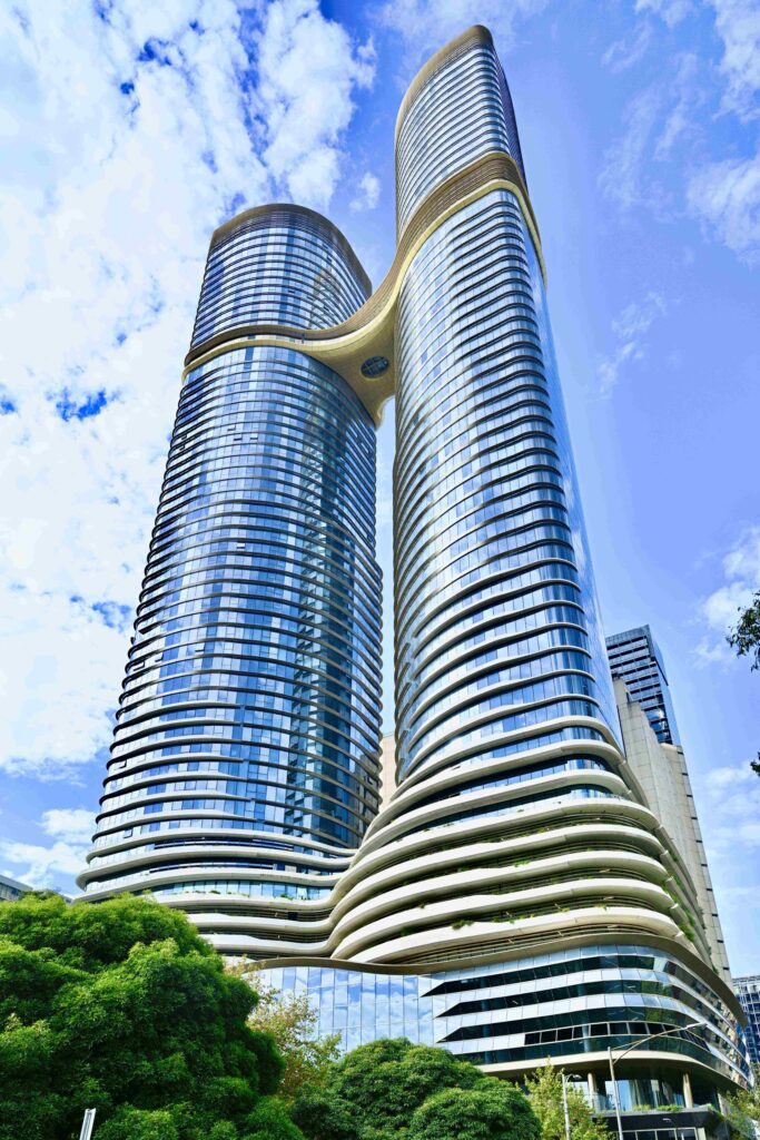 A dramatic, low-angle view of the iconic twin towers of the Melbourne Shangri La, showcasing their futuristic curved glass architecture and connecting sky bridge.