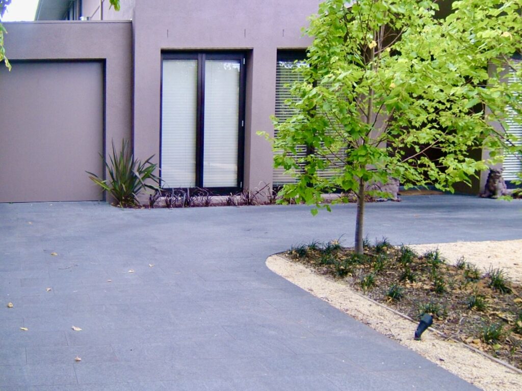 The smooth, dark stone driveway at 2 Otira Road gently curving around a garden bed, complementing the home's minimalist ar