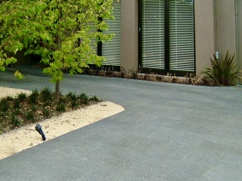A detailed view of the flawlessly laid dark stone pavers from Eigen Stones, showing a clean, curved edge against a garden bed.