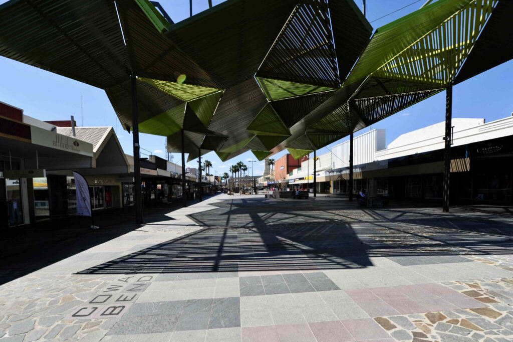 The main promenade of Langtree Mall, showing the multi-toned stone paving from Eigen Stones under the dramatic shadows of a large, green architectural shade structure.