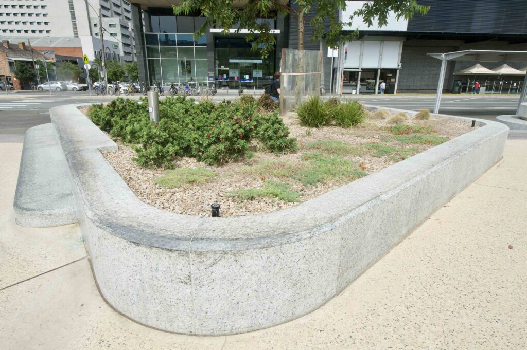 A flowing, curved stone planter wall with a textured finish, creating a soft border for a garden bed in the Uni Square precinct, supplied by Eigen Stones.