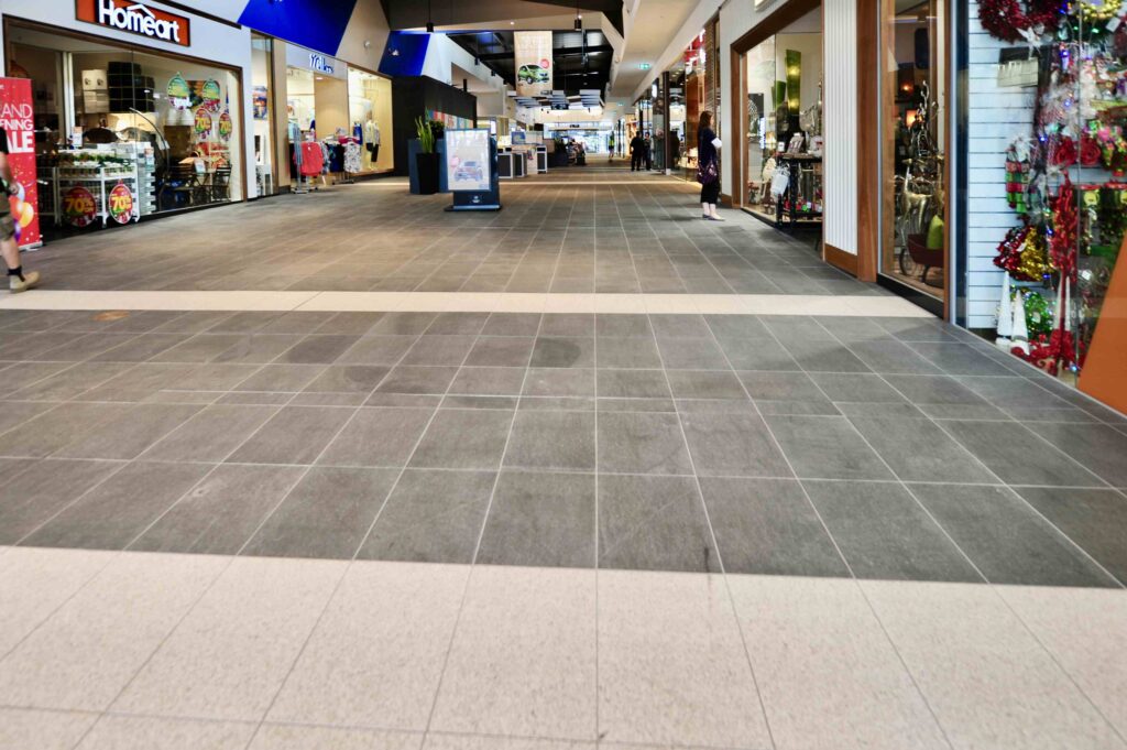 A long retail corridor at Craigieburn Shopping Centre, showcasing the patterned stone floor design with a light central stripe, with all pavers supplied by Eigen Stones.