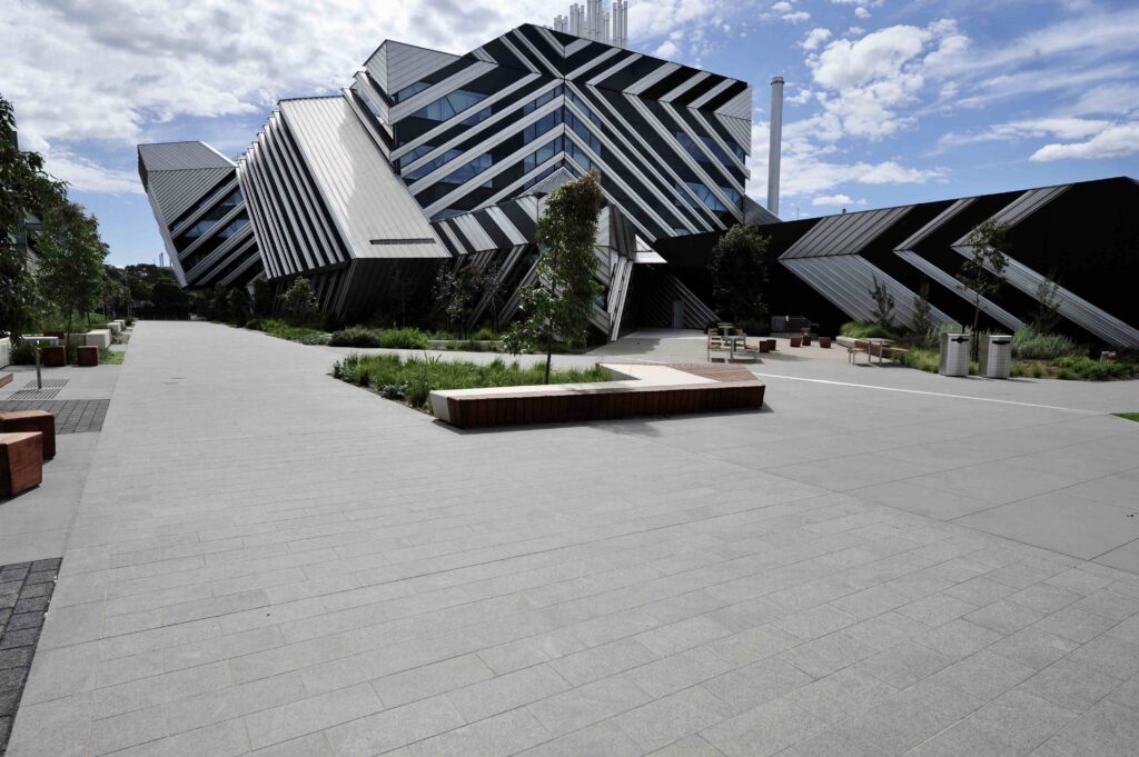 The angular entrance of the Kangan Institute, showing the clean lines of the stone-paved forecourt from Eigen Stones in front of modern timber benches.