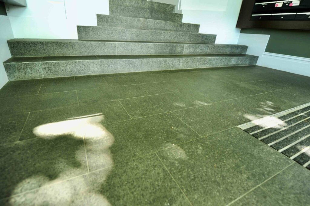 The polished, dark stone floor and stairs in the lobby of 571 Fitzroy Street, creating a sleek and modern atmosphere with materials from Eigen Stones.