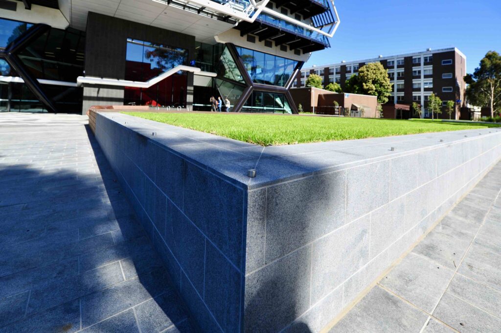 A perspective view of the chevron-patterned stone forecourt at Kangan Institute, with the bold black-and-white facade in the background. Stone supplied by Eigen Stones.